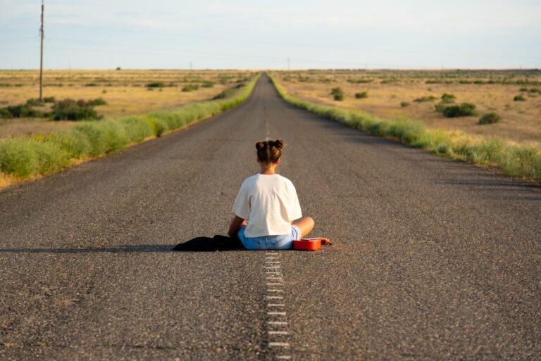 Young girl sitting alone on an empty road, symbolizing reflection and life’s journey