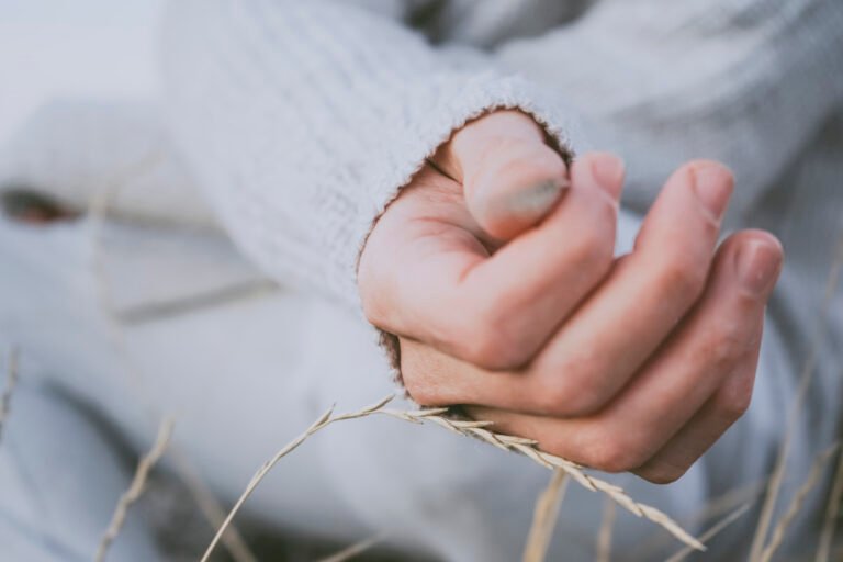 Close-up of a hand gently holding dried grass, symbolizing vulnerability and reflection